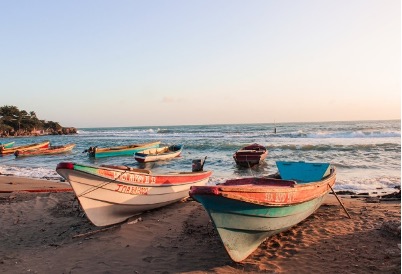 An image of small paddle boats on the shore of the beach and in the water, as the sun is setting.