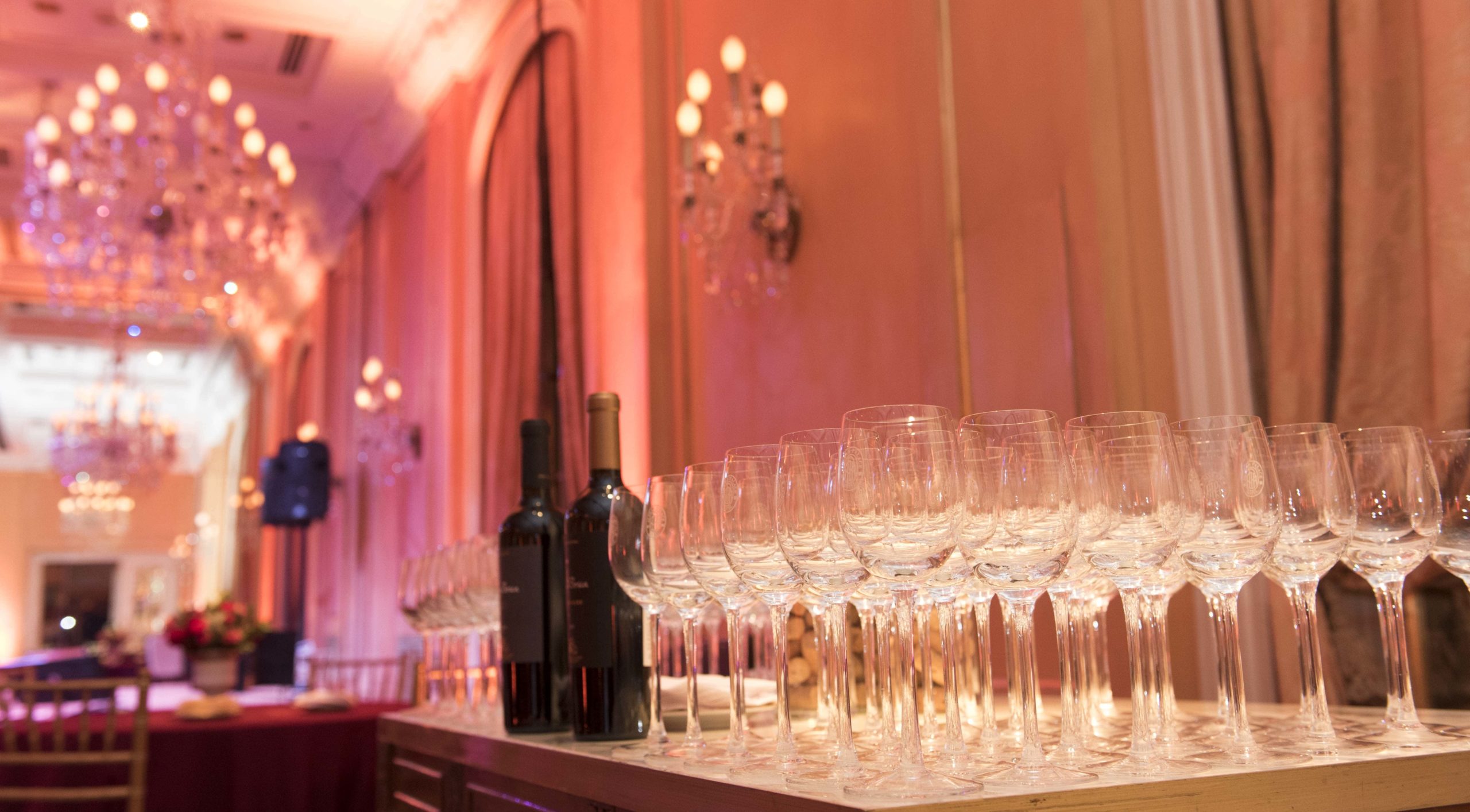 Wine glasses lined up for service in a ballroom with pink and amber lighting