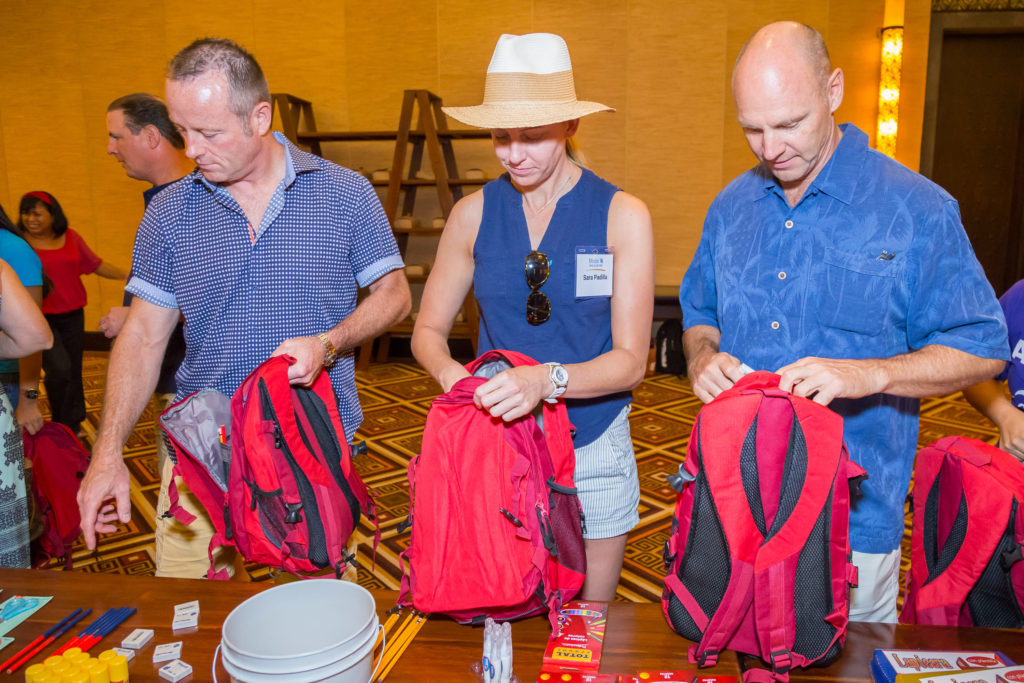 Three CSR event attendees pack red backpacks with school supplies