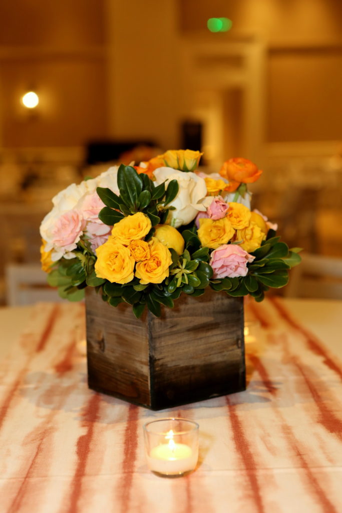 Event table centerpiece in wooden box with yellow, white, and pink flowers