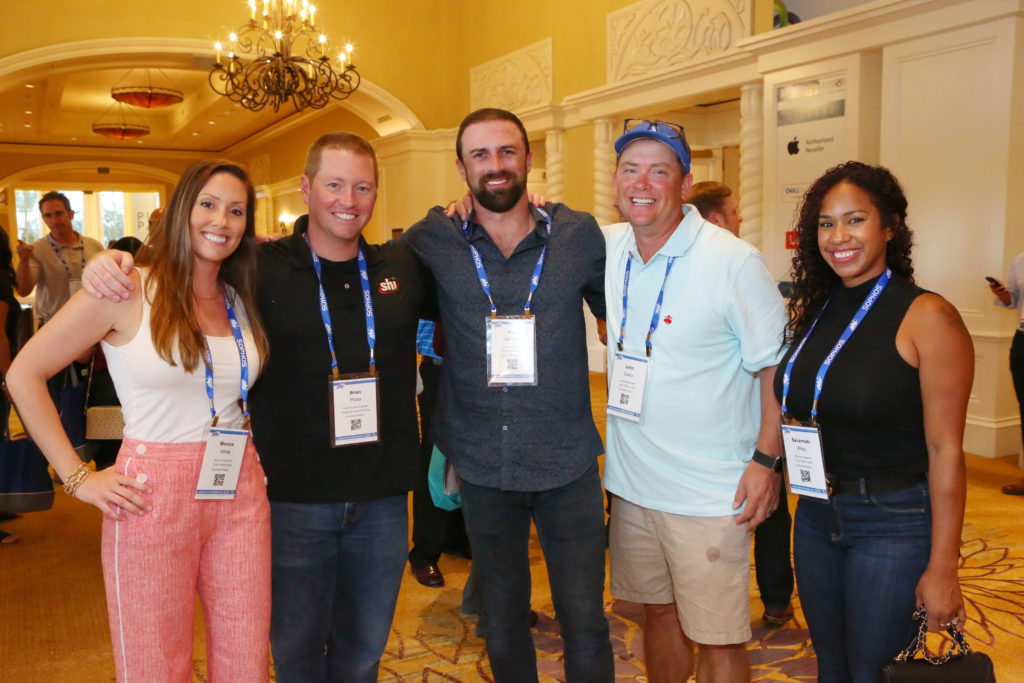 Group of five smiling event attendees outside a hotel ballroom