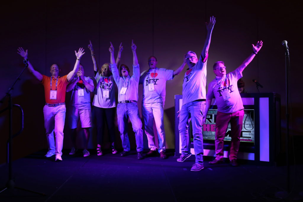 Seven enthusiastic event attendees on stage singing in I heart NY shirts