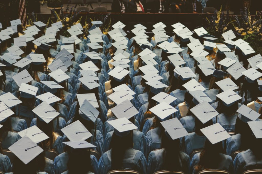 students in graduation caps and gowns face the stage